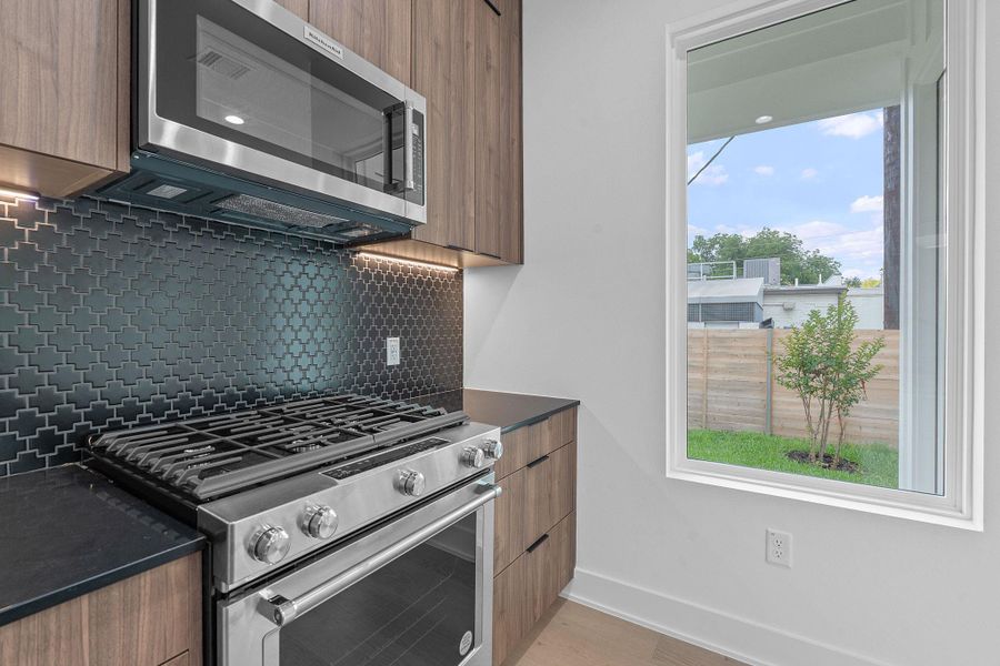 Kitchen featuring appliances with stainless steel finishes, modern cabinets, dark countertops, decorative backsplash, and brown cabinets