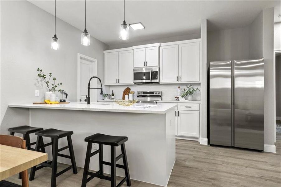 Kitchen with pendant lighting, white cabinets, a kitchen breakfast bar, sink, and appliances with stainless steel finishes