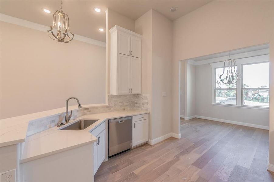 Kitchen with sink, stainless steel dishwasher, light wood-type flooring, decorative light fixtures, and white cabinetry