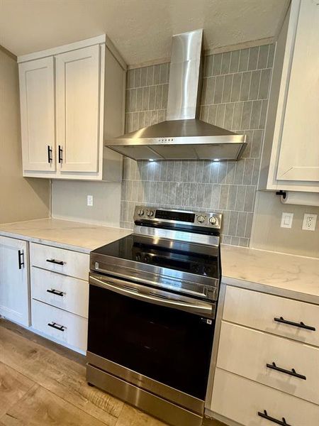 Kitchen featuring stainless steel electric range, light countertops, tasteful backsplash, white cabinetry, and light wood-type flooring Kitchen featuring stainless steel electric range, light countertops, tasteful backsplash, white cabinetry, and light wood-type flooring