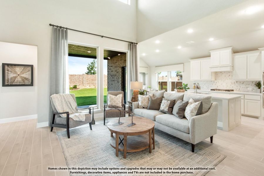 Open-concept living room with high ceilings, gray sofa, and adjacent white kitchen with backyard view Open-concept living room with high ceilings, gray sofa, and adjacent white kitchen with backyard view