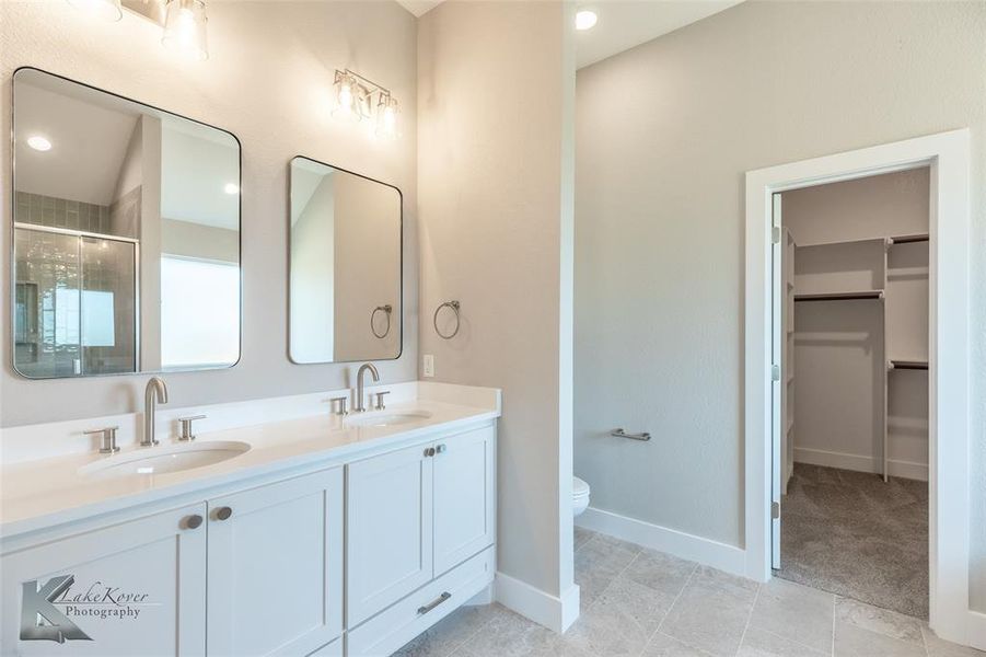 Bathroom featuring double vanity, a stall shower, and a walk in closet