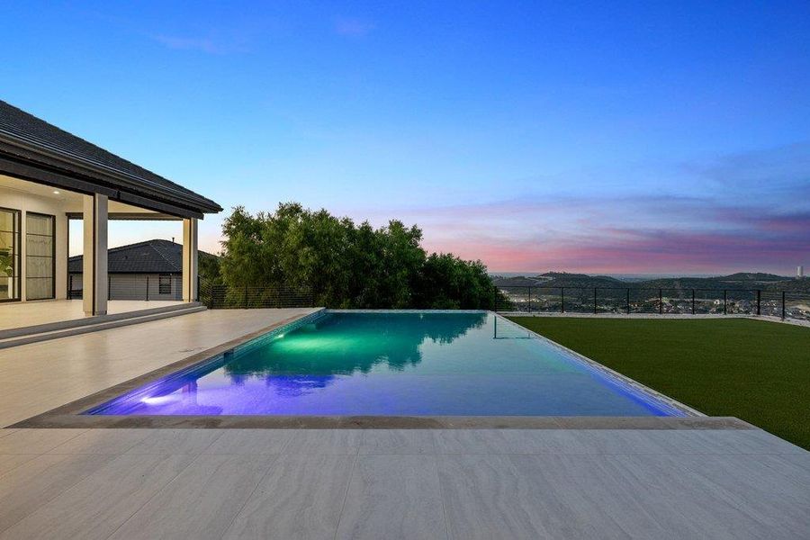An inviting infinity pool shimmers under a colorful twilight sky, offering serene views of the distant landscape.
