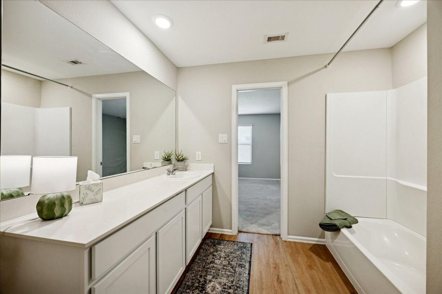 This photo showcases a modern bathroom with a spacious design. It features a long vanity with ample counter space and a large mirror. The bathroom includes a bathtub/Shower with a clean, white finish. The neutral color palette and vinyl flooring create a warm, inviting atmosphere.