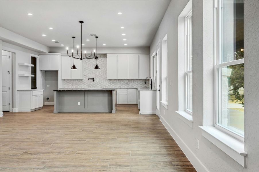 Kitchen with a notable chandelier, a sink, white cabinetry, light wood-style floors, and decorative backsplash