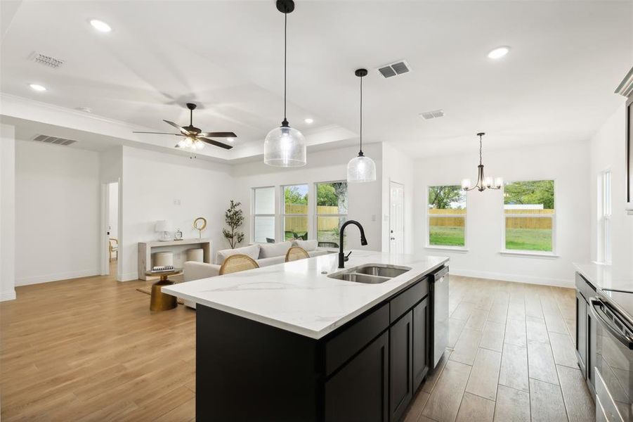 Kitchen with stainless steel appliances, sink, an island with sink, a tray ceiling, and light hardwood / wood-style flooring