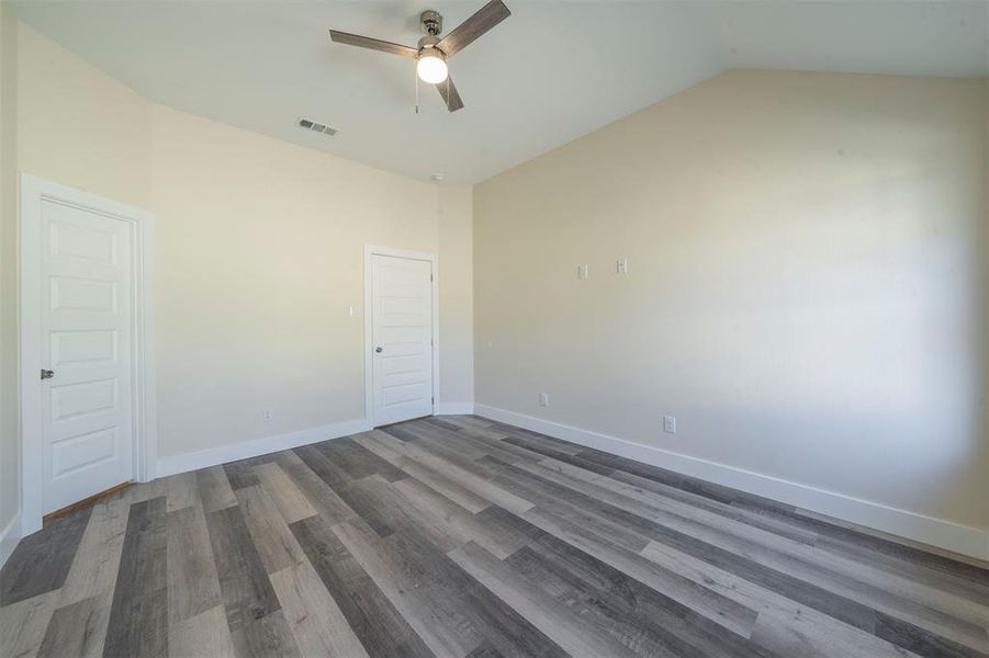 Empty room featuring lofted ceiling, a ceiling fan, visible vents, baseboards, and dark wood finished floors