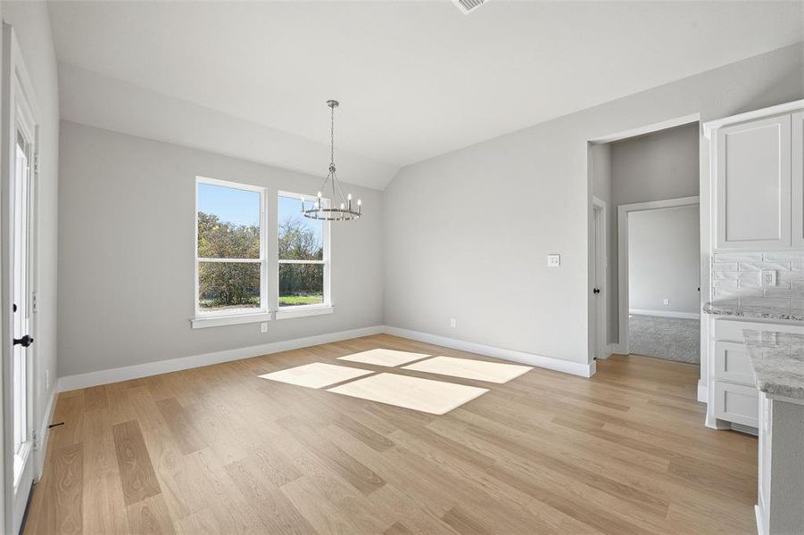 Unfurnished dining area featuring light wood-style floors, vaulted ceiling, and a chandelier Unfurnished dining area featuring light wood-style floors, vaulted ceiling, and a chandelier