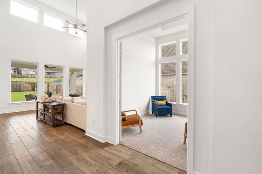 Natural light floods this living area with tall windows and wood flooring, connecting to an inviting carpeted room.
