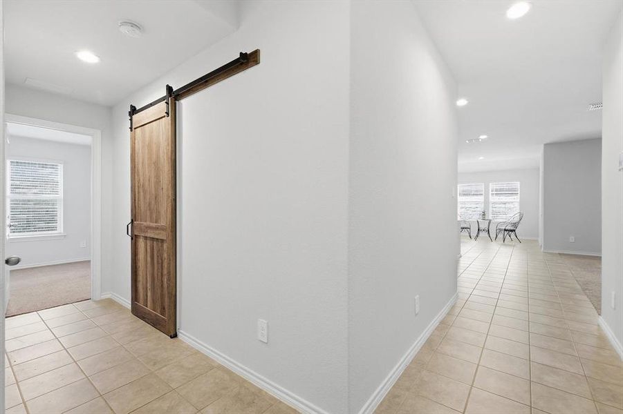 View of laundry, secondary bedroom, barn door, hall to kitchen-living area