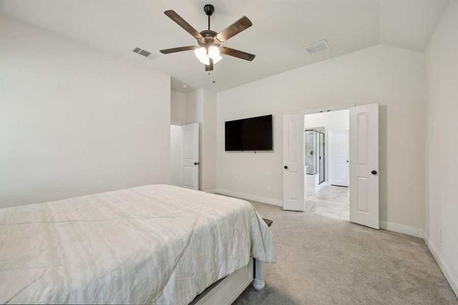 Master bedroom featuring serene views of the property, light colored carpet, neutral paint, multiple windows, and ceiling fan.