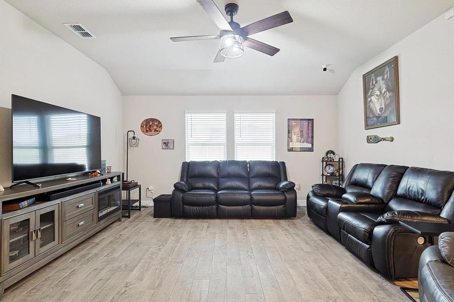 Living room featuring baseboards, visible vents, a ceiling fan, vaulted ceiling, and light wood-style floors