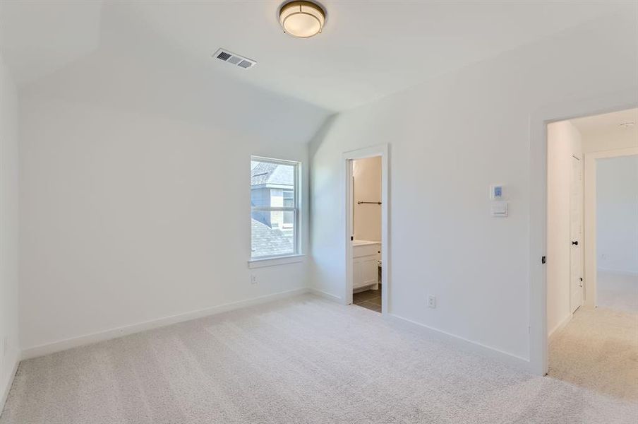 Unfurnished bedroom featuring light carpet, a spacious closet, vaulted ceiling, ensuite bathroom, and a closet