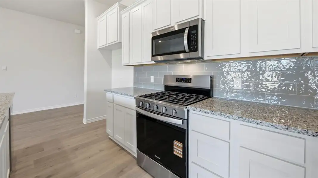 Kitchen with appliances with stainless steel finishes, white cabinets, and light stone countertops