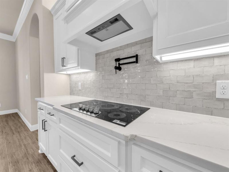 Kitchen with black electric stovetop, crown molding, light hardwood / wood-style floors, light stone counters, and white cabinetry