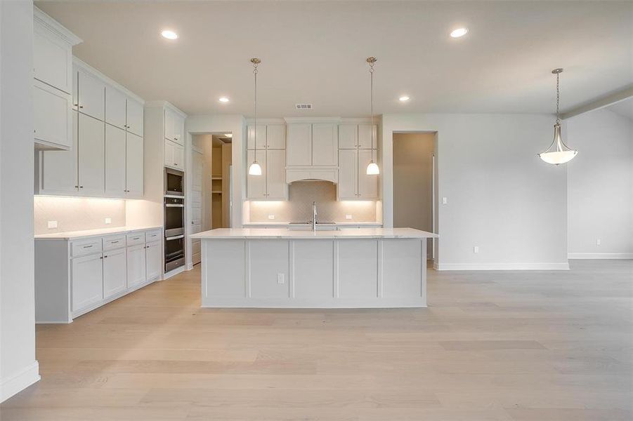 Kitchen with light hardwood / wood-style floors, sink, decorative backsplash, and decorative light fixtures