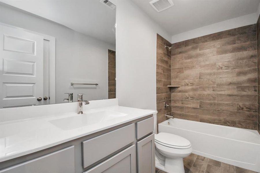 Experience sophistication in the secondary bathroom, where tile flooring complements a bath/shower combo with tile surround. Slate wood cabinets complete with a beautiful light countertop, enhances the space for a truly inviting ambiance. Sample photo of completed home. As-built color and selections may vary.