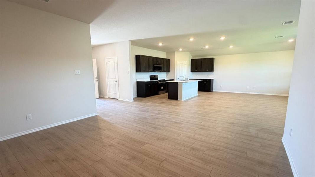 Expansive open-concept living area featuring wood-finish flooring, recessed lighting, and a kitchen island with a light-toned countertop