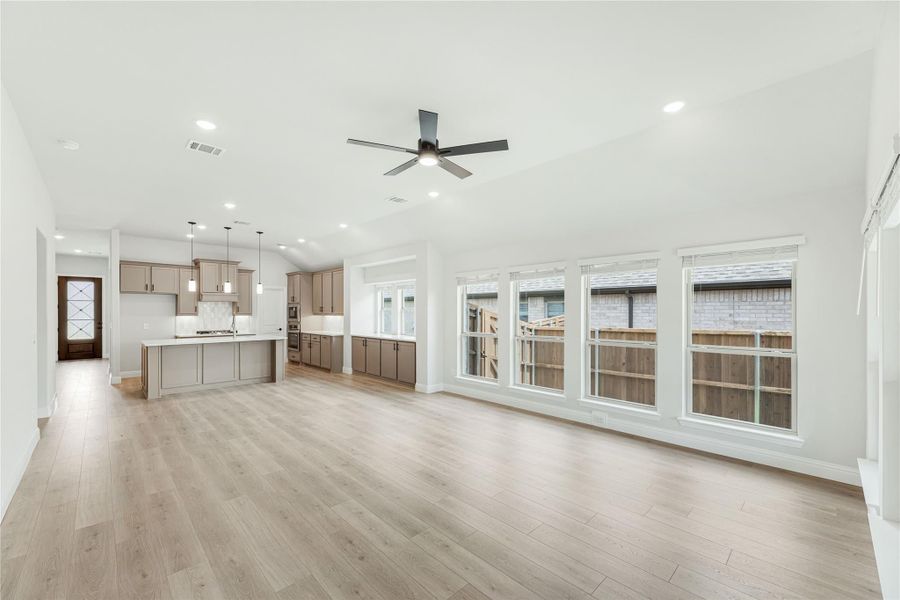 Open living area with light wood floors, ceiling fan, and kitchen with gray cabinets and island in background
