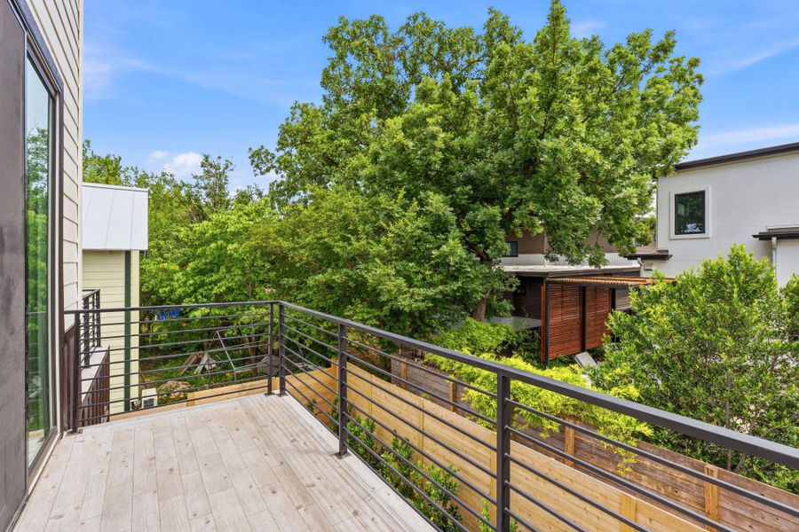 Balcony with wood-finish flooring and black metal railings, offering tree canopy surroundings