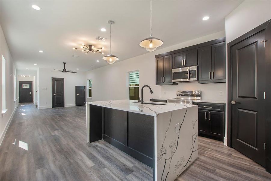 Kitchen featuring hanging light fixtures, wood-type flooring, light stone countertops, ceiling fan, and stainless steel appliances