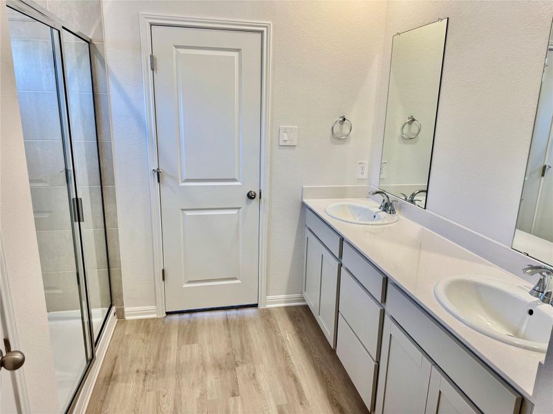 Full bathroom with double vanity, a stall shower, and light wood-style floors