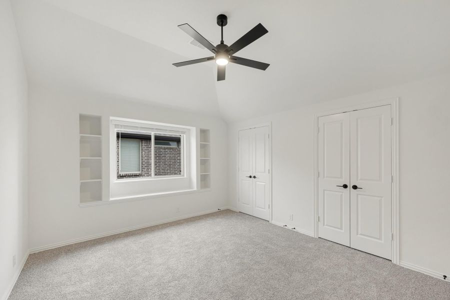 Empty bedroom with vaulted ceiling, black ceiling fan, built-in shelves, and two white double doors