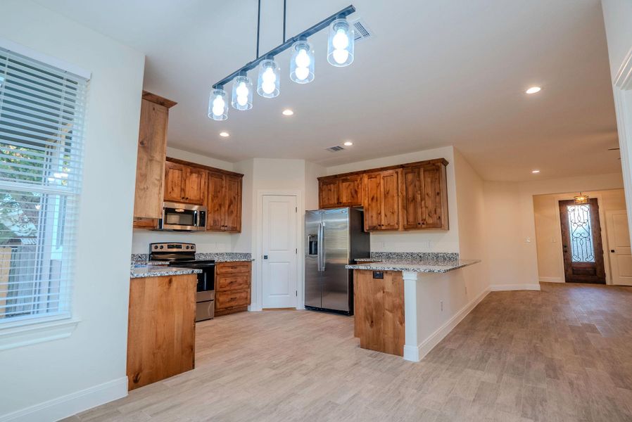 Kitchen featuring hanging light fixtures, light stone countertops, brown cabinets, stainless steel appliances, and a peninsula Kitchen featuring hanging light fixtures, light stone countertops, brown cabinets, stainless steel appliances, and a peninsula
