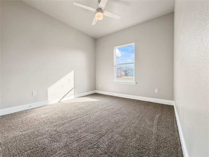 Empty room featuring carpet flooring, a textured wall, and a ceiling fan Empty room featuring carpet flooring, a textured wall, and a ceiling fan