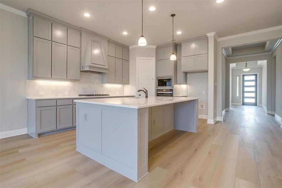 Kitchen with appliances with stainless steel finishes, crown molding, light hardwood / wood-style flooring, and premium range hood