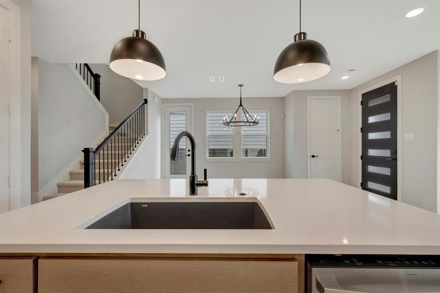 Kitchen featuring light stone countertops, a center island with sink, dishwasher, and hanging lights