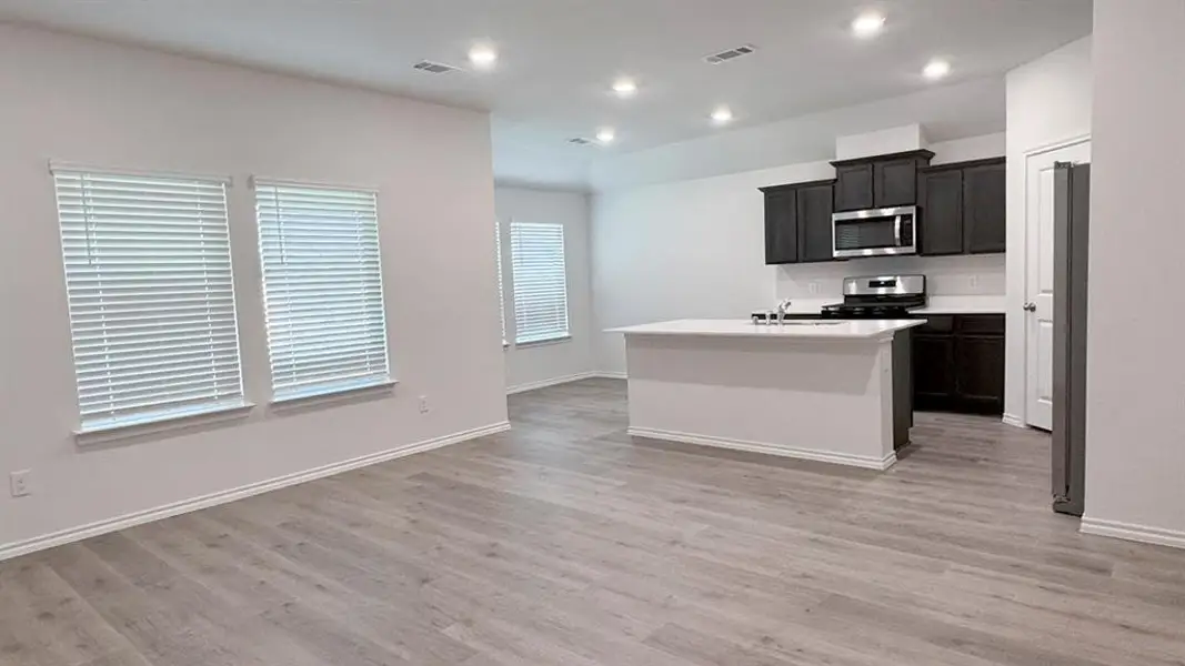 Kitchen with a center island with sink, stainless steel appliances, light wood-type flooring, dark cabinets, and recessed lighting