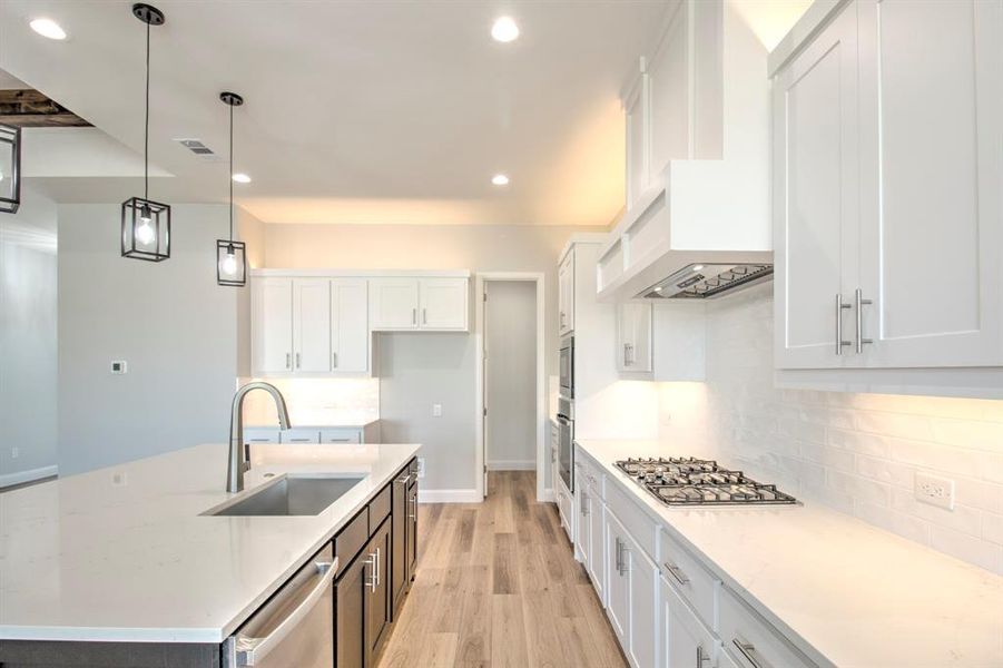 Kitchen featuring white cabinets, decorative light fixtures, sink, and appliances with stainless steel finishes