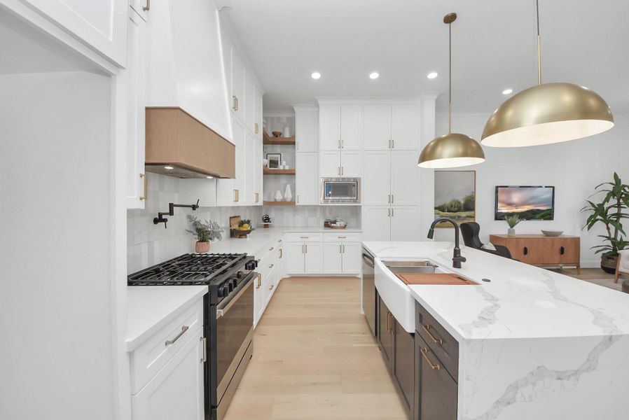This modern kitchen invites you to cook and entertain with sleek white cabinetry, a spacious marble island, stainless steel appliances, and brass pendant lights. The open layout flows into the living area, creating a bright and functional space for gatherings.