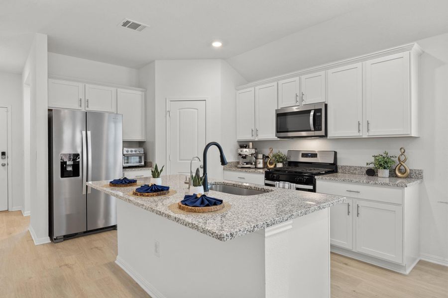 Kitchen with stainless steel appliances, white cabinets, light stone countertops, light wood-style floors, and a kitchen island with sink