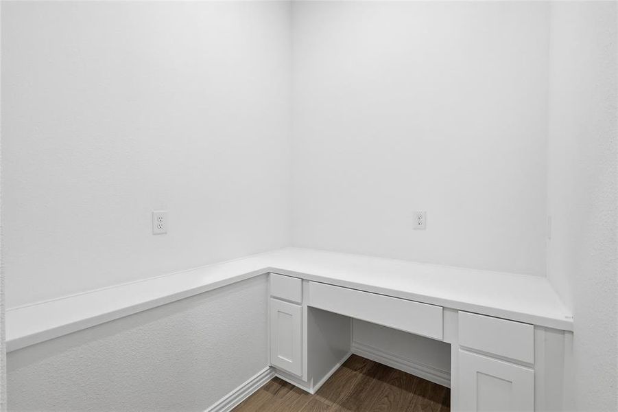 Dedicated workspace featuring a built-in desk with white cabinetry, a spacious white countertop, and wood-finish flooring