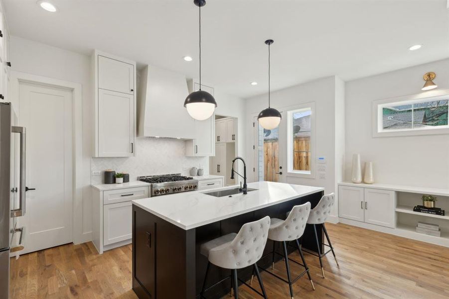 Kitchen with premium range hood, pendant lighting, an island with sink, white cabinets, and sink