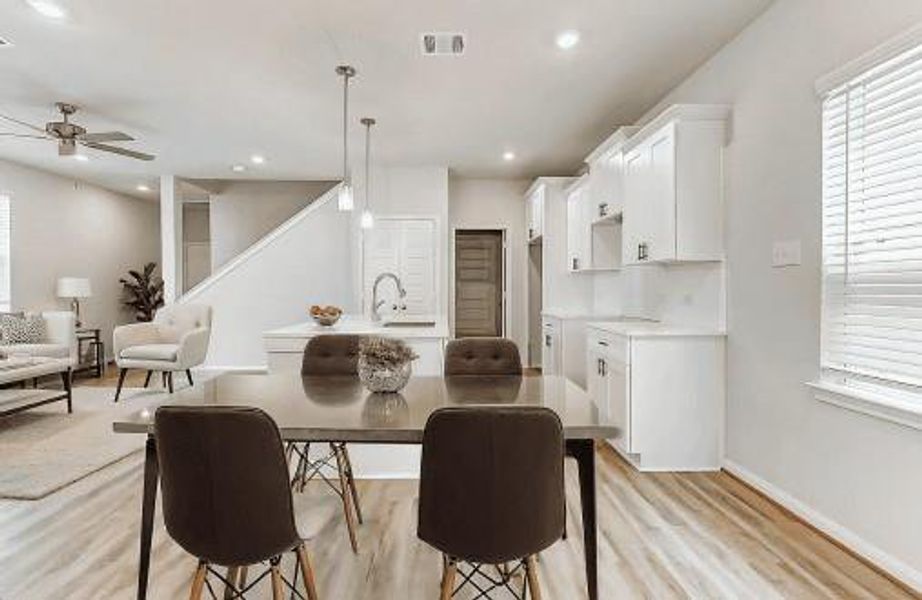 This photo showcases a modern, open-concept living space with a dining area, kitchen, and living room. The kitchen features white cabinetry and a sleek island. The dining area features great space to entertain. Light wood-look floors and neutral walls add to the bright and spacious feel, complemented by recessed lighting and natural light from the windows.The image is not the actual home; it is a home with the same floor plan in the neighborhood. Finishes may vary. This photo showcases a modern, open-concept living space with a dining area, kitchen, and living room. The kitchen features white cabinetry and a sleek island. The dining area features great space to entertain. Light wood-look floors and neutral walls add to the bright and spacious feel, complemented by recessed lighting and natural light from the windows.The image is not the actual home; it is a home with the same floor plan in the neighborhood. Finishes may vary.