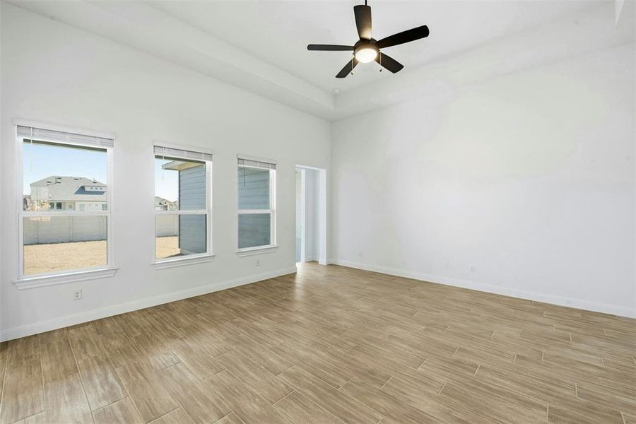 Spacious room featuring wood-finish flooring, white walls, and a tray ceiling with a black ceiling fan