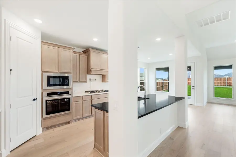 Kitchen with light wood cabinets, stainless steel appliances, dark countertop island, and light hardwood floors