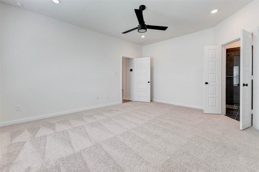 Another view of the primary suite highlights its impressive scale and clean, modern design. The open layout provides flexibility for furniture placement, while the doorway leads seamlessly to the luxurious ensuite bathroom. Bright, airy, and thoughtfully designed, this space offers a peaceful escape at the end of the day with plenty of room to unwind.