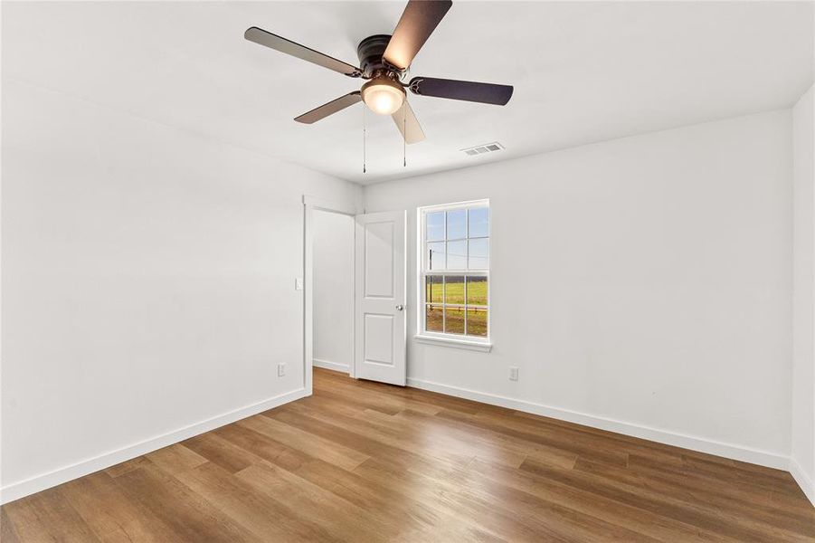 Room featuring wood-finish flooring, white walls, a ceiling fan with integrated lighting, and a window overlooking a green landscape