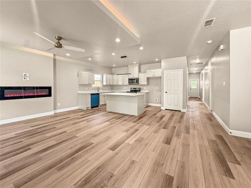 Open-concept living space featuring wood-finish flooring, a contemporary electric fireplace, and recessed lighting Open-concept living space featuring wood-finish flooring, a contemporary electric fireplace, and recessed lighting