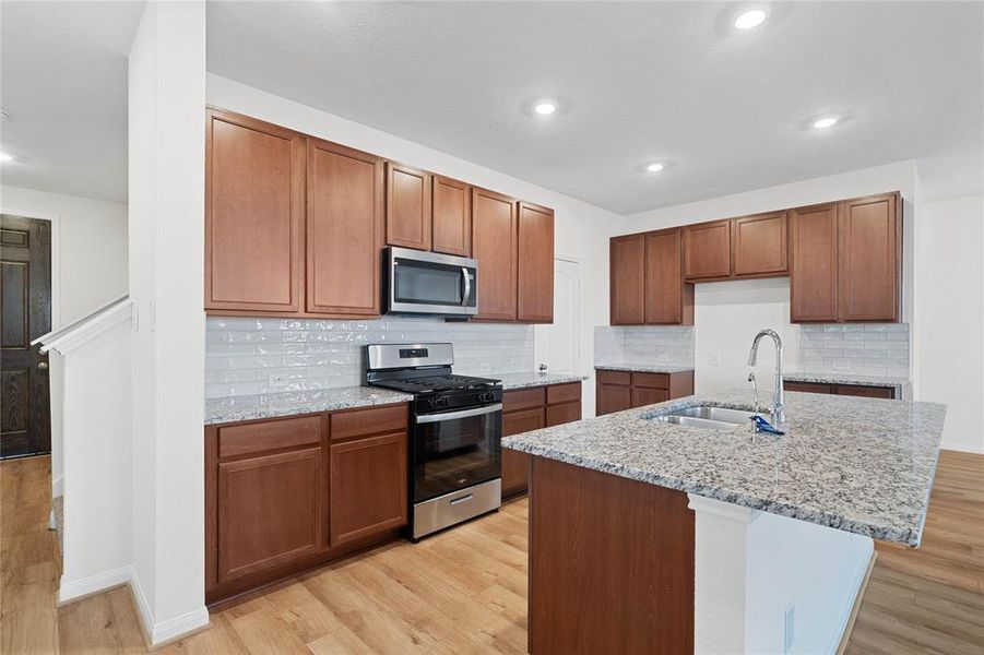 This spacious kitchen features high ceilings, stained wood cabinets, granite countertops, SS appliances, modern tile backsplash, recessed lighting, large kitchen island with space for a breakfast bar, large windows with privacy blinds, and a pantry all overlooking your huge family room.