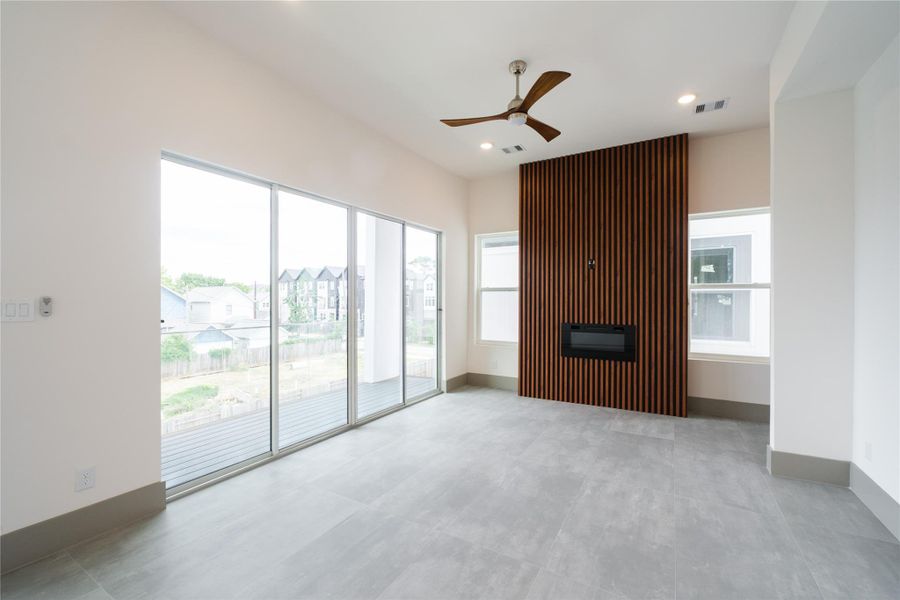 Representative Middle Level Living Space View (Design selections and colors may vary): Anchored by a modern electric fireplace and full-height slat accent walls, the sun-splashed living area offers a sophisticated yet relaxed space. Oversized sliding glass doors provide seamless indoor-outdoor flow to the balcony. Large cement-like gray tiles flooring is one of the select upgrades incorporated into a different unit.