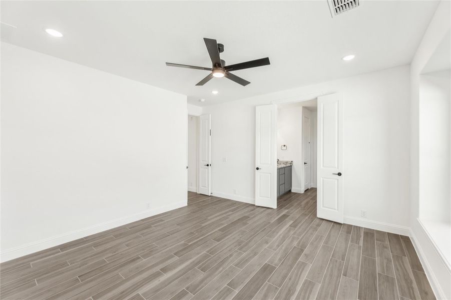 Empty bedroom with wood-look tile floors, black ceiling fan, and doorway leading to ensuite bathroom Empty bedroom with wood-look tile floors, black ceiling fan, and doorway leading to ensuite bathroom