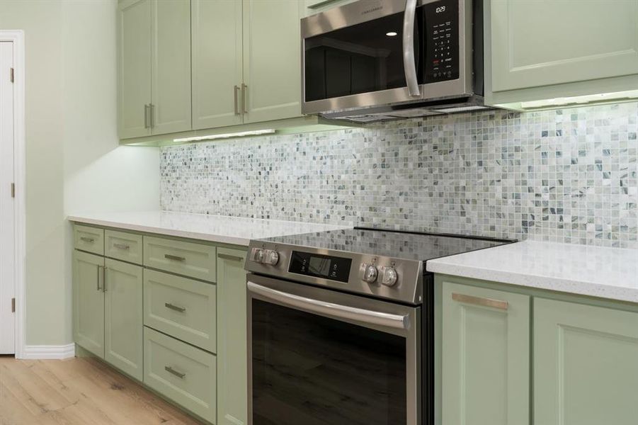 Kitchen featuring green cabinets, light stone counters, appliances with stainless steel finishes, and light wood-type flooring