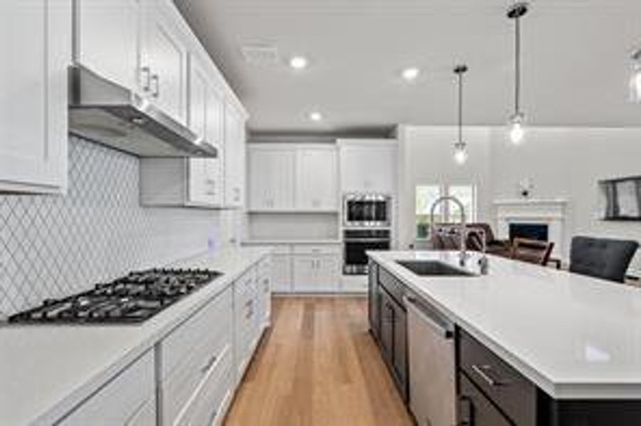 Kitchen featuring a center island with sink, white cabinetry, hanging light fixtures, and appliances with stainless steel finishes