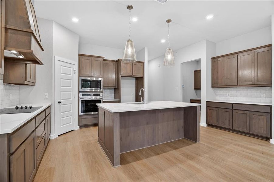 Kitchen featuring wood-finish flooring, an oversized island with a built-in sink, pendant lighting, stainless steel appliances, and extensive cabinetry