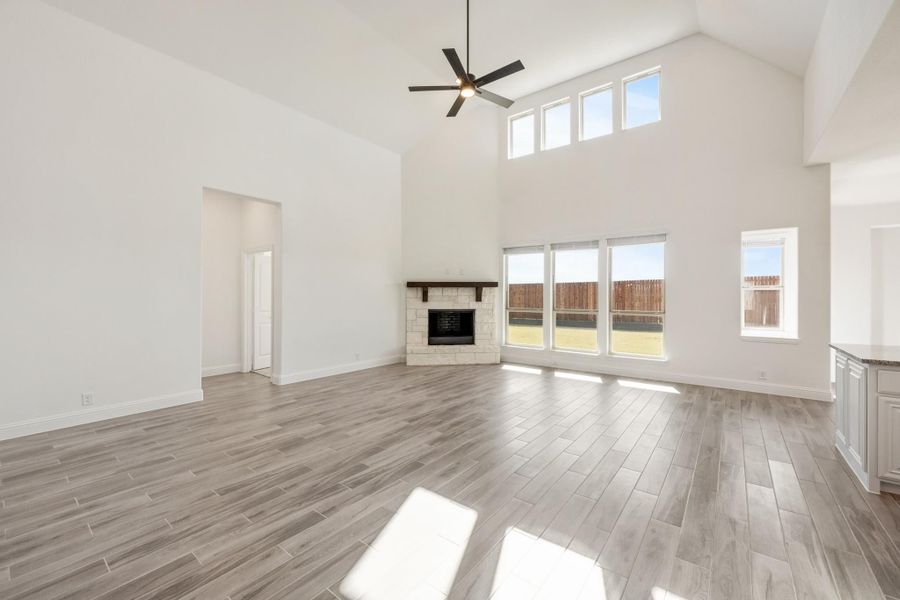 Open living room with vaulted ceiling, stone fireplace, ceiling fan, and wood-look tile floors Open living room with vaulted ceiling, stone fireplace, ceiling fan, and wood-look tile floors